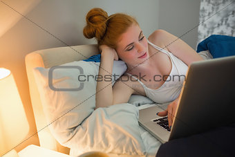 Pretty redhead lying on her bed using laptop