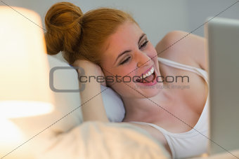 Laughing redhead lying on her bed using laptop