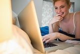Cheerful redhead lying on her bed using laptop