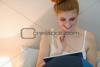 Cheerful redhead using digital tablet sitting on her bed