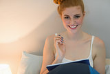 Happy redhead using digital tablet sitting on her bed