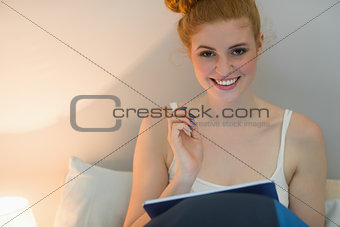 Happy redhead using digital tablet sitting on her bed