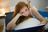 Pretty redhead using digital tablet lying on her bed