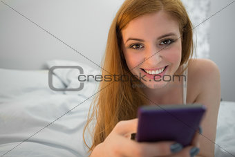 Smiling redhead lying on bed sending a text
