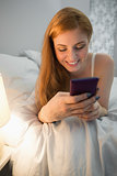 Cheerful redhead lying on bed sending a text