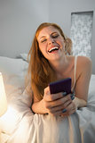 Laughing redhead lying on bed sending a text