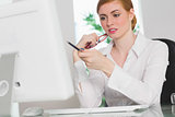 Frowning businesswoman working at her desk holding glasses