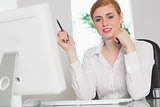 Stern businesswoman working at her desk holding pen