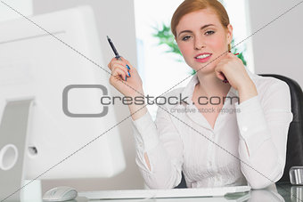 Stern businesswoman working at her desk holding pen