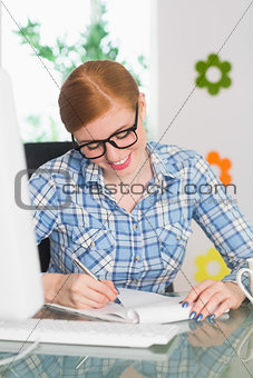 Happy redhead writing on notepad at her desk