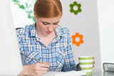 Focused redhead writing on notepad at her desk and holding coffee
