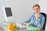 Cheerful redhead sitting at her desk smiling at camera