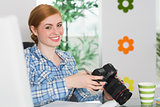 Happy photographer sitting at her desk holding her camera