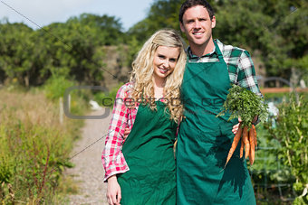 Cute couple posing in their garden holding carrots