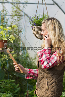 Happy woman holding a clipboard in her green house on the phone