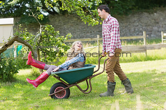 Handsome man pushing his laughing girlfriend in a wheelbarrow