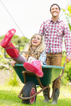 Smiling man pushing his laughing girlfriend in a wheelbarrow