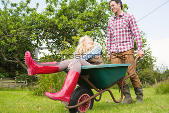 Cheerful man pushing his laughing girlfriend in a wheelbarrow