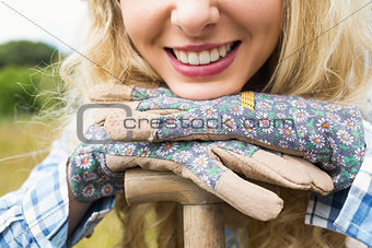 Cheerful blonde woman leaning on a shovel wearing gardening gloves