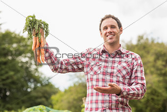 Young man wearing a check shirt presenting some carrots