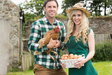 Smiling young couple holding chicken and basket of eggs