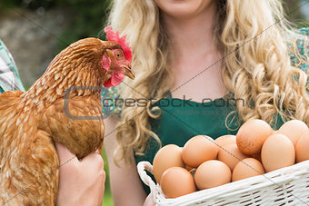 Young couple holding chicken and basket of eggs