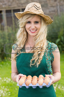 Young smiling blonde woman holding carton of eggs
