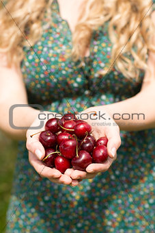 Close up of a blonde woman holding some cherries