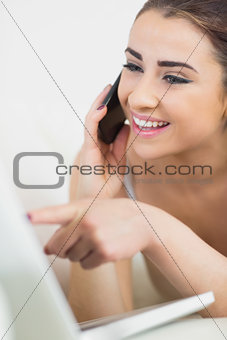 Happy young woman phoning while using her laptop
