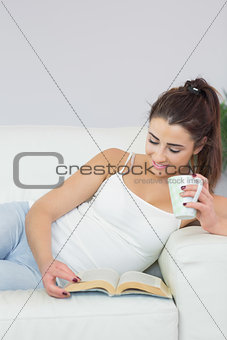 Amused pretty woman reading a book and having coffee