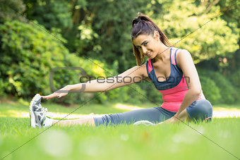 Pretty sporty woman stretching her leg and smiling at camera