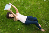 Happy young woman lying on a lawn using her tablet