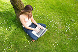 Cute woman leaning against a tree using her notebook