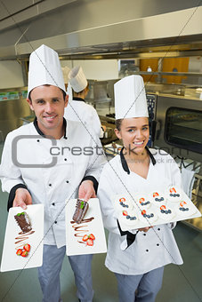 Two young chefs presenting dessert plates
