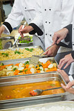 Chefs standing at serving trays of vegetables sauce and pasta