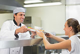 Young happy chef handing a plate to the waitress