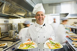 Mature head chef presenting proudly two dinner plates