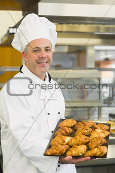 Baker showing some croissants on a baking tray