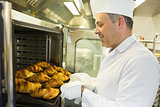 Mature baker putting some croissants into an oven