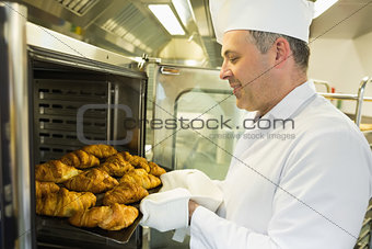 Mature baker putting some croissants into an oven
