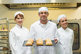 Young male baker holding a baking tray with rolls on it