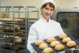 Happy female baker showing some rolls on a baking tray
