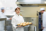 Cute female baker holding a baking tray with rolls on it