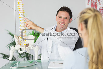 Smiling doctor showing a patient something on skeleton model