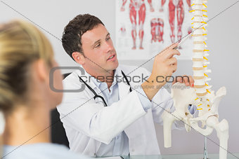 Good looking doctor showing a patient something on skeleton model