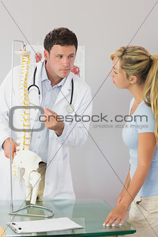 Calm doctor showing a patient something on skeleton model