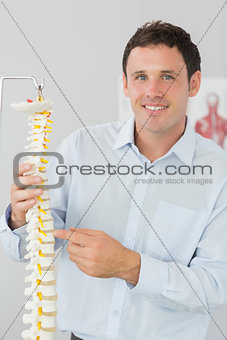 Handsome cheerful doctor pointing at skeleton model