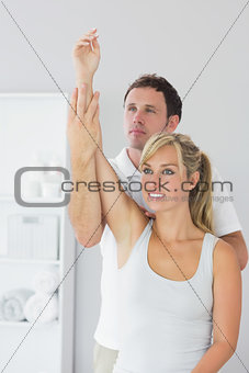 Handsome physiotherapist controlling patients arm