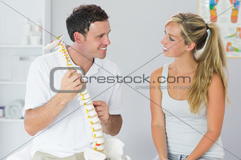 Smiling physiotherapist showing patient something on skeleton model