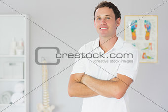 Handsome happy physiotherapist standing with arms crossed